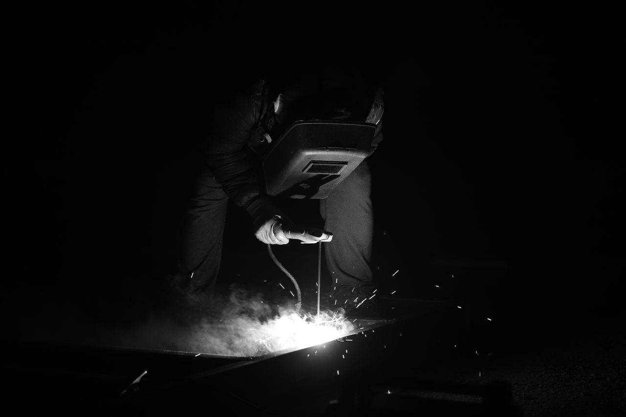 Home Black and white photo of a welder working with sparks flying in a dark setting.